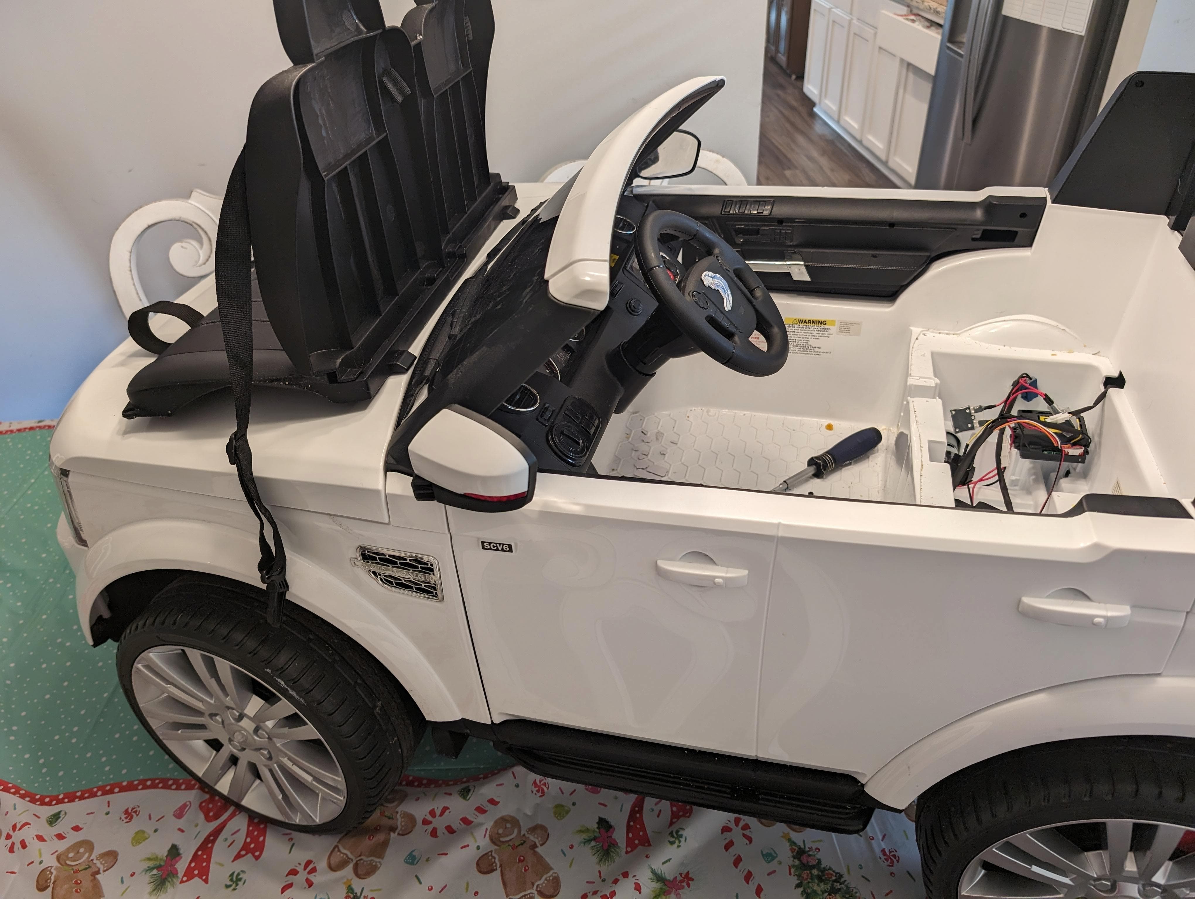 Coche eléctrico infantil blanco abierto con herramientas y cables visibles durante cambio de batería.